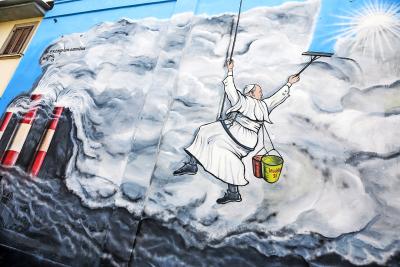 Graffitikunstenaar Mauro Pallotta maakte in 2019 in Albano (Italië) deze muurschildering: paus Franciscus hangt als een bergbeklimmer aan een touw en veegt de vervuilende rook van een fabriek weg. Op zijn emmertje staat ‘Laudato Si’. © KNA
