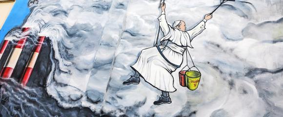 Graffitikunstenaar Mauro Pallotta maakte in 2019 in Albano (Italië) deze muurschildering: paus Franciscus hangt als een bergbeklimmer aan een touw en veegt de vervuilende rook van een fabriek weg. Op zijn emmertje staat ‘Laudato Si’. © KNA